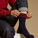 Le modèle porte des chaussettes hautes bleu marine à rayures rouges, style sport pour homme.