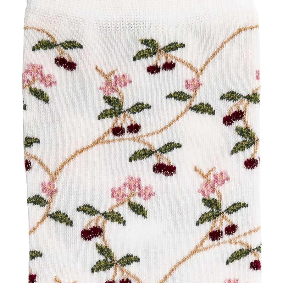 Détail motifs cerises rouges et fleurs roses sur chaussette femme mi-haute blanche.